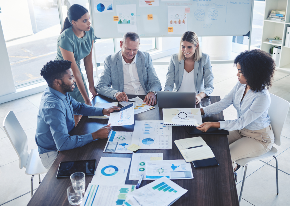 Equipo de trabajo reunido alrededor de una mesa compartiendo informes financieros y gráficos de desempeño corporativo.